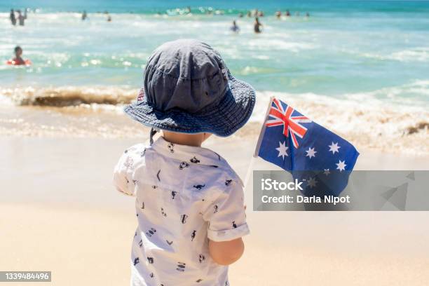 Little Boy Wearing Hat Holding Australian Flag On A Sandy Ocean Beach Australia Day Concept Stock Photo - Download Image Now