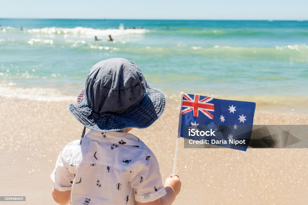 Little boy wearing hat holding Australian flag on a sandy ocean beach. Australia Day concept Little boy wearing hat holding Australian flag on a sandy ocean beach. Australia Day celebration concept 18-23 Months Stock Photo