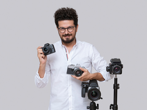 Photographer posing with digital and analogue cameras over gray background, Studio shot