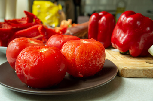 Scalded tomatoes, peeled on a plate, red peppers on a wooden board