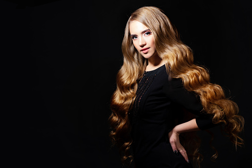 Luxurious golden curls, portrait of a young beautiful woman with beautiful hair, black background copy space on the left