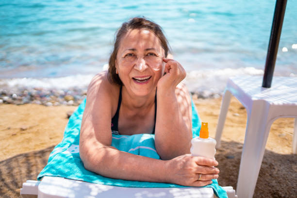 istock Senior woman applying sunscreen on her face and smiling while sunbathing on the beach 1339496690