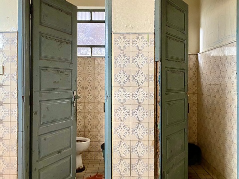 Front view of public restroom cabinet doors. Antique construction. Wooden doors are more closed in left cabin and open in right side, creating a kind of gradient