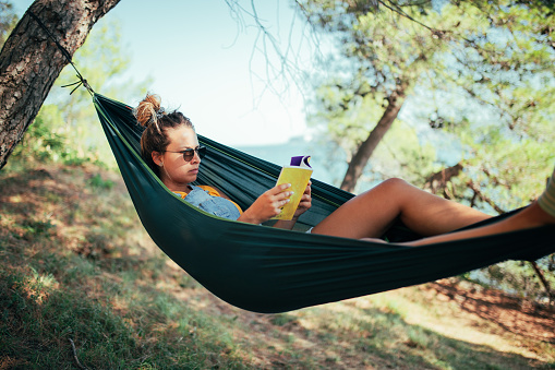 An image depicting a young woman enjoying her vacation. She's in remote woods, lying in a hammock and enjoying the surrounding.