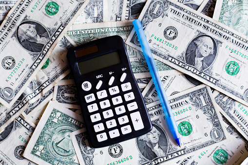 Background of US One Dollar Bills.  Calculator and pen  represent the need for small families to the government to budget wisely in trying times.