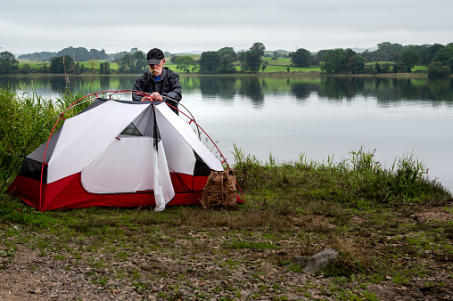 Retired man wild camping alone beside a Scottish lake on an overcast late summer morning