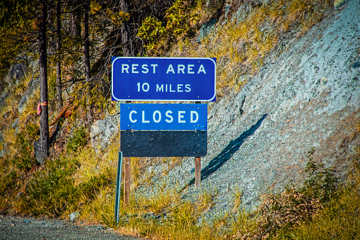 Rest Area sign with Closed posted below it on side of USA road by a steep incline in Autumn
