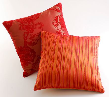 Couple of red and orange cushions with line and flower patterns, isolated