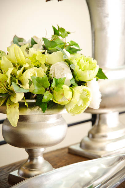 istock Silver vase on a table setting, with white and green plastic flowers 1339520859