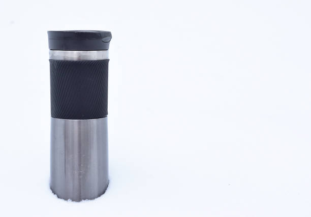 Thermos mug stands in a deep snowdrift. Contrast of pure white snow with a dark object.