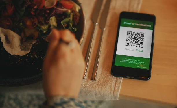 istock Woman in restaurant with certificate of immunization on smartphone. Status is valid. 1339533486