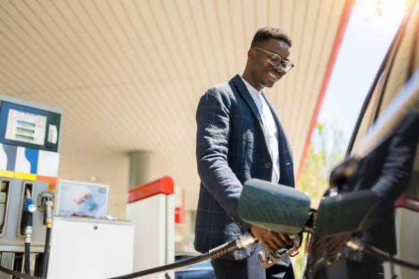 glücklicher junger afroamerikaner, der sein auto an der tankstelle betankt. - füllen stock-fotos und bilder