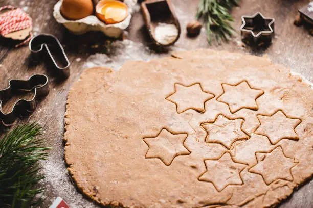 Close-up of star shapes on flattened dough. Various cookie cutters are on table. It is in kitchen at home.