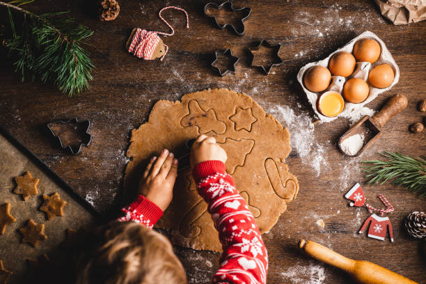 Boy cutting dough with christmas cookie cutters on table Directly above view of boy cutting dough with cookie cutters. Male child is preparing Christmas sweets at table. He is wearing red sweater with long sleeves. baking stock pictures, royalty-free photos & images