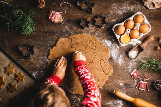 Directly above view of boy cutting dough with cookie cutters. Male child is preparing Christmas sweets at table. He is wearing red sweater with long sleeves.