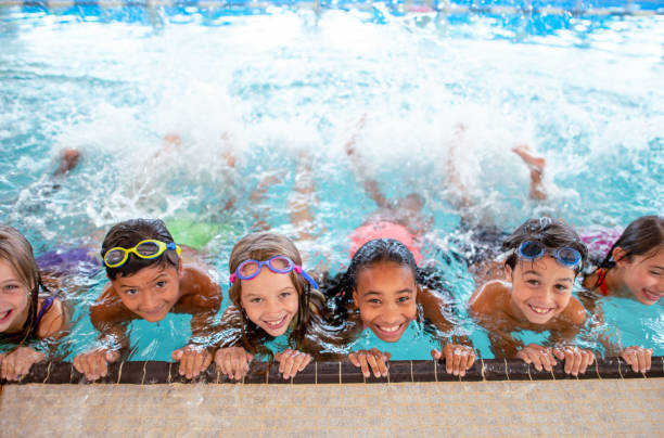 Multi ethnic group of children learning to kick in the swimming pool A multi ethnic group of elementary age children at in the pool during swimming class. They are smiling at the camera while holding onto the side of the pool and kicking their legs to create splashes. swimming stock pictures, royalty-free photos & images