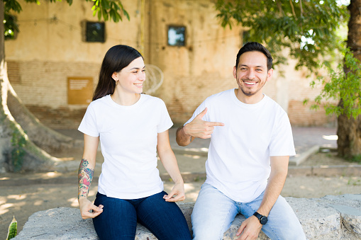 Cheerful young woman gifting her boyfriend matching print t-shirts. Latin woman pointing to her white t-shirt