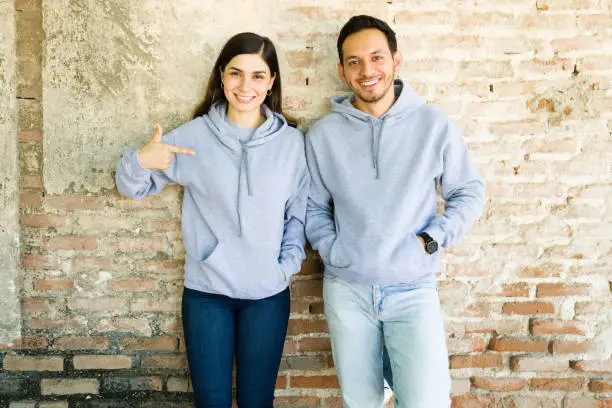 Loving our new hoodies. Good-looking young couple pointing to the print design on their sweatshirts