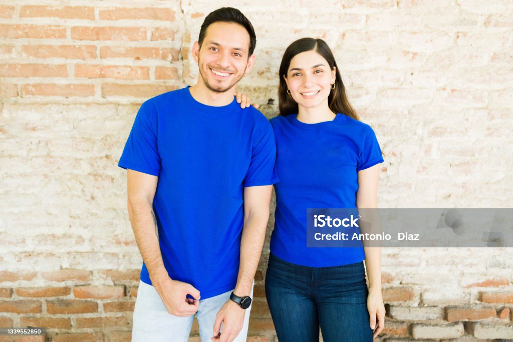 Portrait of a woman and man with mock-up t-shirts Hispanic young couple with blue matching print t-shirts making eye contact while standing outdoors Blue Stock Photo