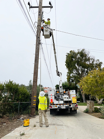 Electrician in bucket of articulated boom lift is repairing electrical transmission on power poles against blue sky background