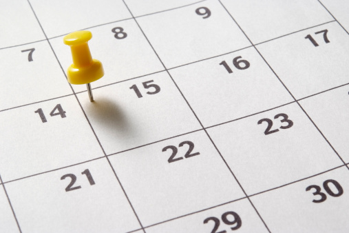 Close-up shot of yellow thumbtack in calendar with shadow.