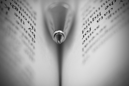 A blue ball pen embedded in an open book. Concept of education, study, research. Macro with shallow depth of field.