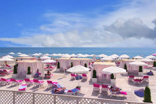 Sea beach on a sunny day, tourists sunbathe in the sun and lie under the umbrellas, Sochi, Russia.