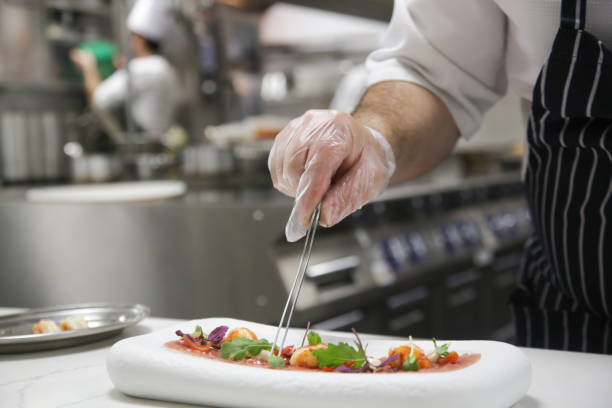 istock Chef in restaurant garnishing fish carpaccio. Chef preparing dish in kitchen. Decorating dish, close up. 1339592624