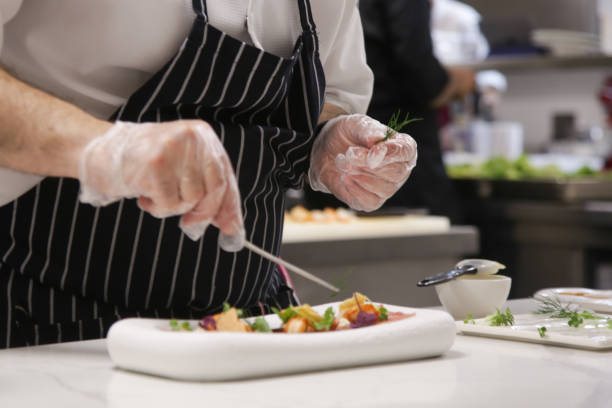 istock Chef in restaurant garnishing fish carpaccio. Chef preparing dish in kitchen. Decorating dish, close up. 1339592685