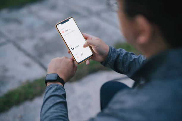 vue par-dessus l’épaule homme chinois asiatique utilisant l’application mobile de suivi de la condition physique se connectant au tracker de fitness au parc public après l’exercice le matin - medical check photos et images de collection