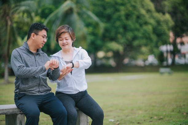 couple asiatique chinois mi-adulte utilisant l’application mobile de suivi de la condition physique se connectant au tracker de fitness au parc public après l’exercice le matin au banc du parc - medical check photos et images de collection