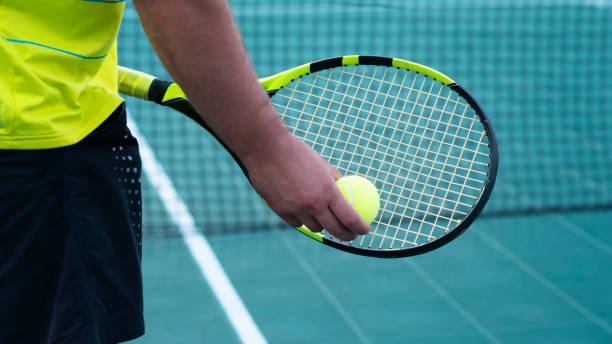 Close-up of tennis racket and yellow ball. Tennis player holds a tennis racket. Sports background. Copy space. A tennis player waiting to serve during a match. Male athlete plays tennis on a professional tennis court. Active Lifestyle. Tennis sport. tennis tournament stock pictures, royalty-free photos & images