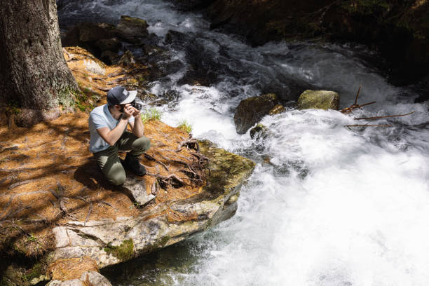 Young photographer taking photos of the raging water torrent in the mountains