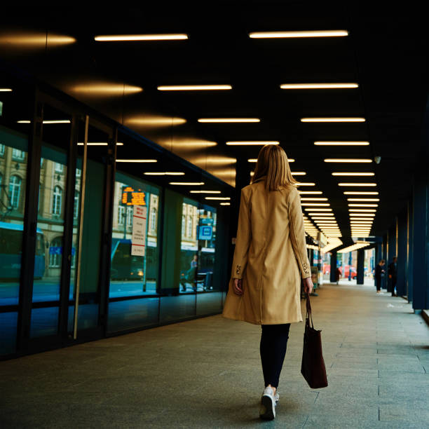 kobieta w płaszczu spaceruje po ulicy miejskiej z torbą - people in a row in a row business office worker zdjęcia i obrazy z banku zdjęć