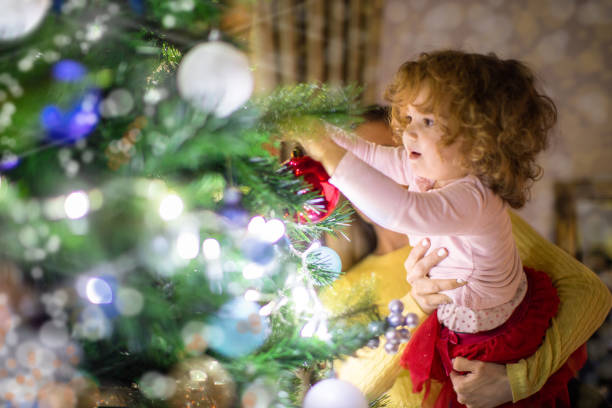 Mother and daughter celebrate New Year next to the Christmas tree. They have fun decorating the Christmas tree with beautiful decorations and glowing lanterns