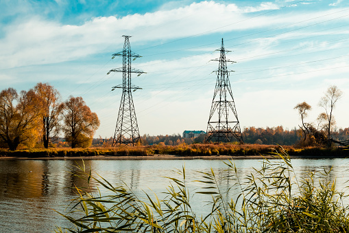 High-voltage power lines crossing the river. High voltage power transmission towers on the background of an autumn landscape.