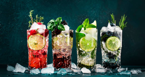 Cocktails drinks. Classic alcoholic long drink or mocktail highballs with berries, lime, herbs and ice on blue background stock photo