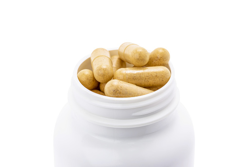 Close-up of brown herbal supplement capsules for health inside white plastic bottle isolated on white background
