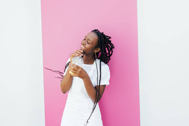 istock Happy woman drinking juice while dancing at white wall with pink stripe 1339619395