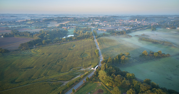 Aerial view of landscape at dawn in Denmark. Autumn and fog hanging low. Looking down at the clouds. Road into small town