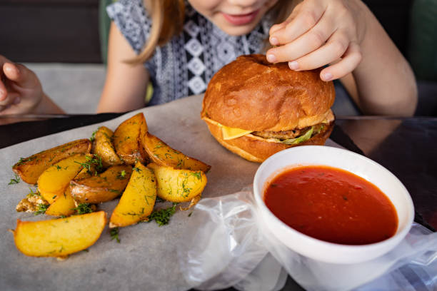 a little girl with gloves eats a burger and potatoes in a summer outdoor cafe.