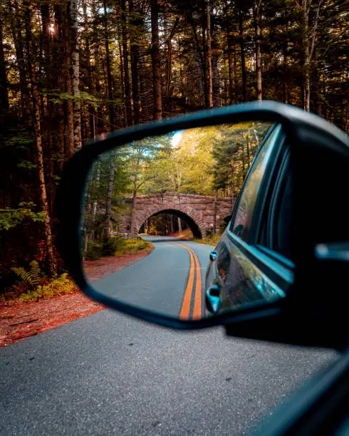An old, historic bridge in Acadia National Park through the side mirror of a Honda Passport.