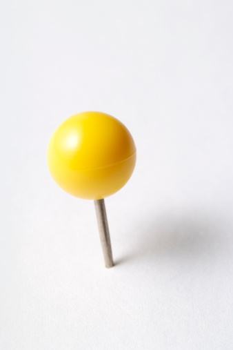 Close-up shot of yellow thumbtack isolated on white background.