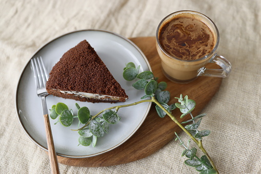 Istanbul, Turkey-August 15, 2021: Cup of coffee with milk and slice of cocoa cake on wooden cutting board. There is a green branch around the plate. Shot with Canon EOS R5.