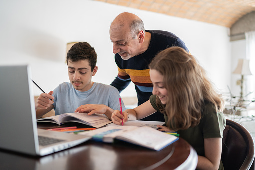 Father helping son and daughter with homework at home
