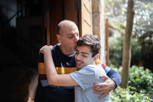 Father embracing and kissing teenager son at home