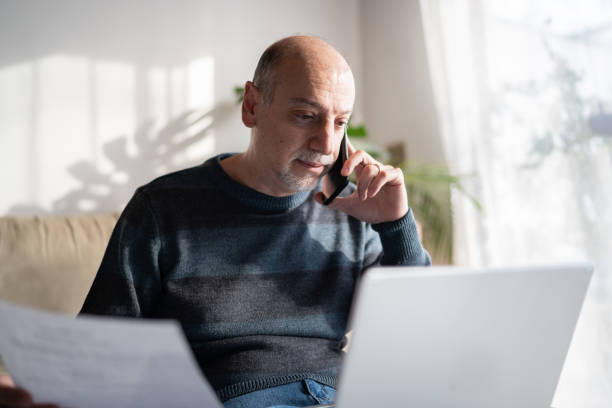 istock Mature man talking on the phone and using laptop at home 1339635324