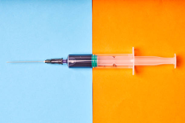 istock Medical disposable syringe with blue liquid on orange-blue background 1339639589