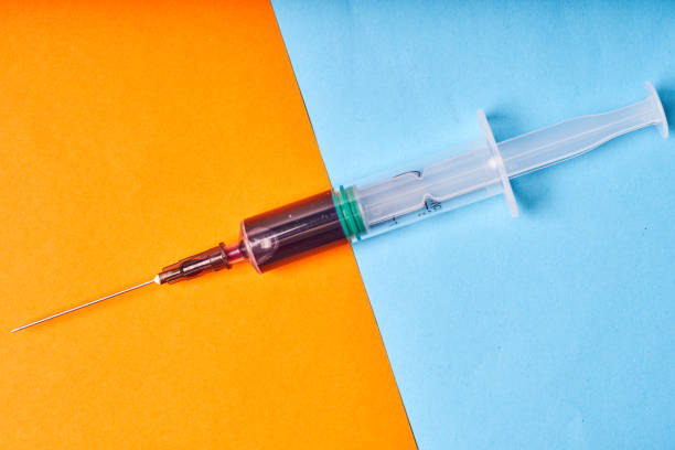istock Medical disposable syringe with blue liquid on orange-blue background 1339639594