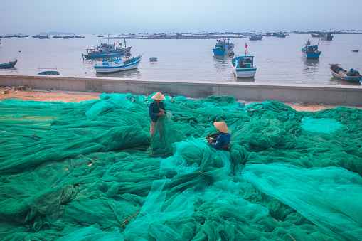 High angle view of 2 men is knitting fishing net on a large beautiful turquoise fishing net by the beach in Van Ninh town, Khanh Hoa province, central Vietnam